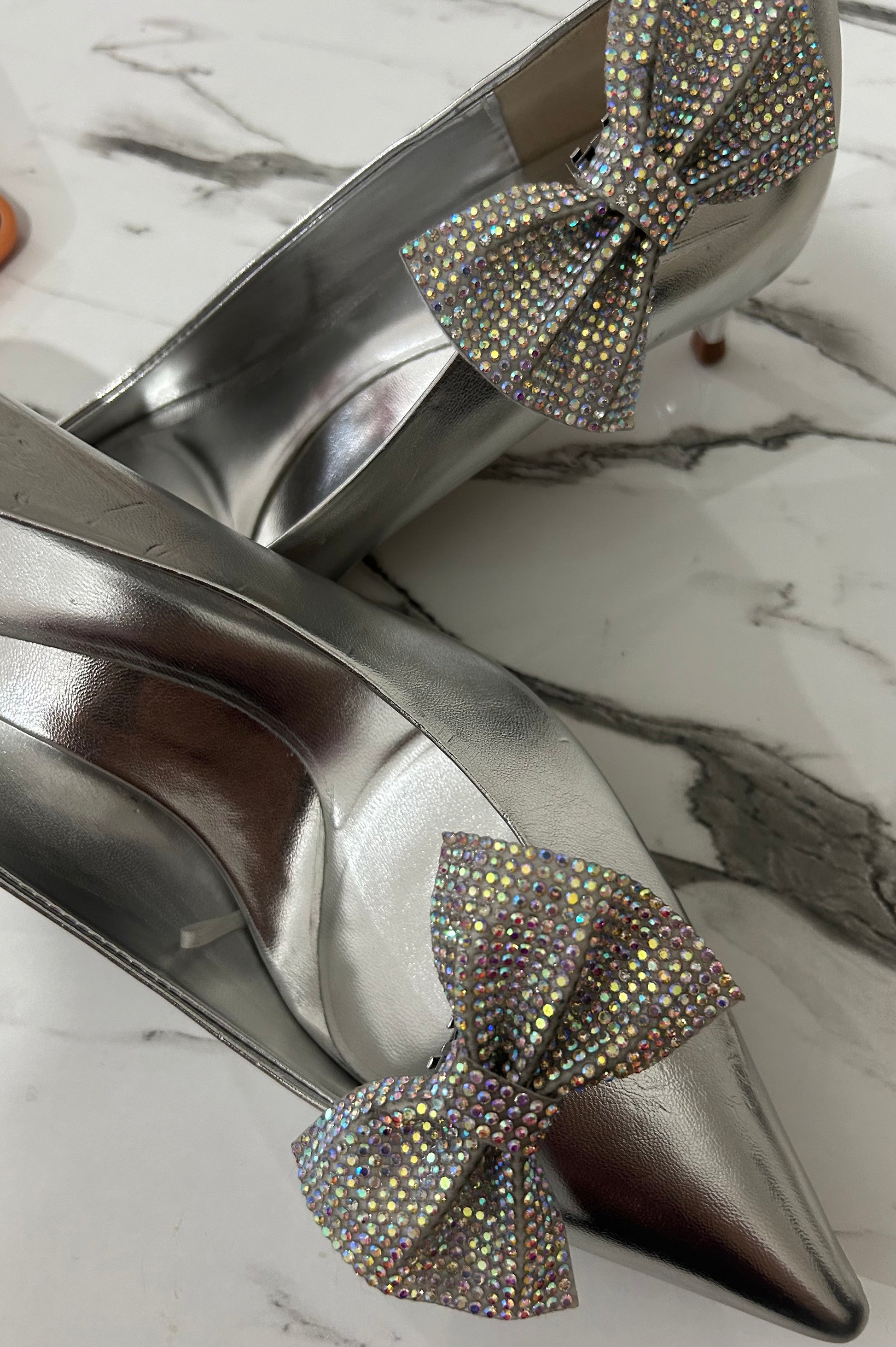 Silver high-heeled shoes with rhinestone bows on a marble surface